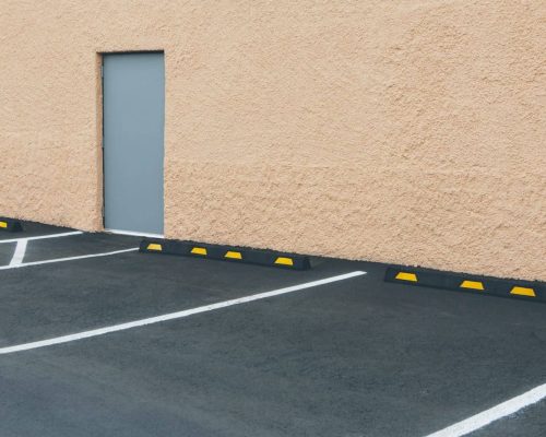 A car park with lined bays outside a building, and a door in a wall.