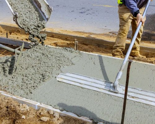 Construction worker pour cement for sidewalk in concrete works with mixer truck with wheelbarrow at