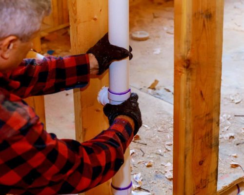 Plumber installing PVC pipe at plastic drain pipe under construction of the house